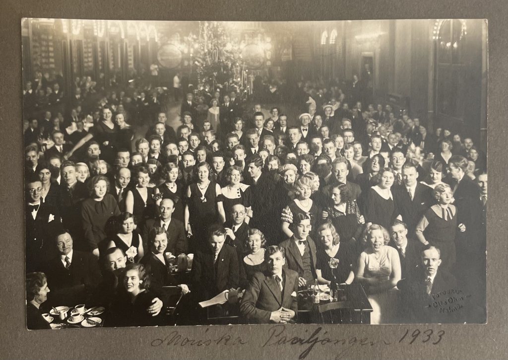 Foto ur ett gammalt fotoalbum, enligt stämpel i högra hörnet är det taget på Moriska paviljongen 1933 av fotograf Otto Ohm. På bilden syns ett hundratal unga, finklädda människor som ler mot kameran. 